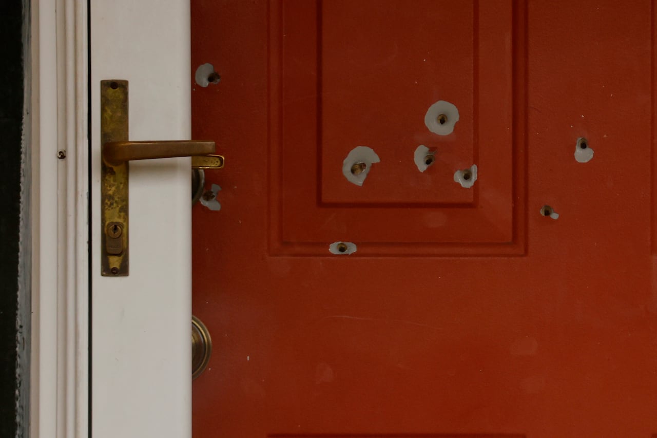 A red front door of a residence is shown with several bullet holes in it.