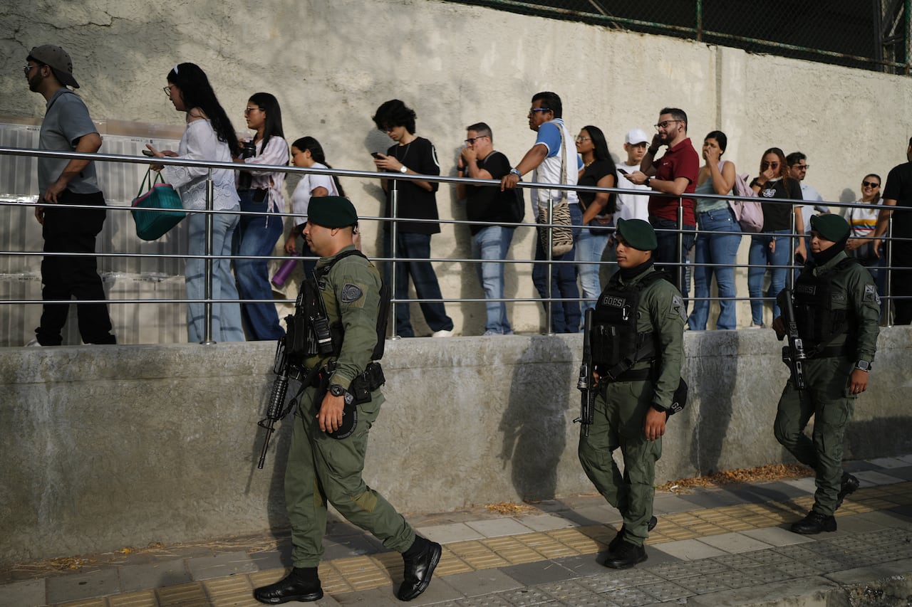 Soldiers patrol as people wait in line.