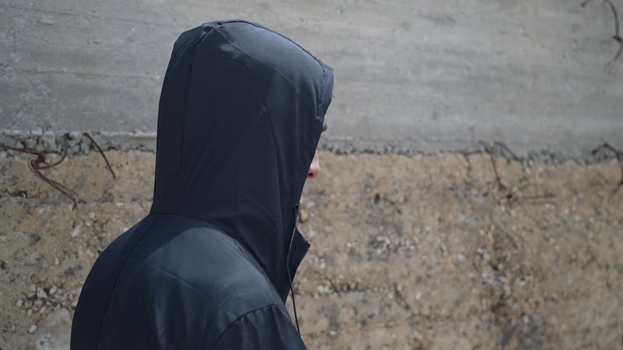 A boy in a black jacket stands with his hood up.