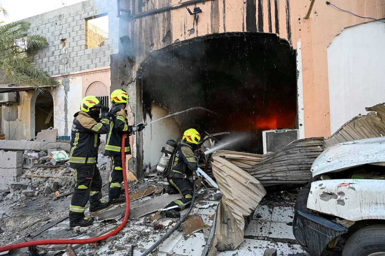 A handful of firefighters utilize a hose near the entrance of a street-level building, with large amounts of debris on the ground.