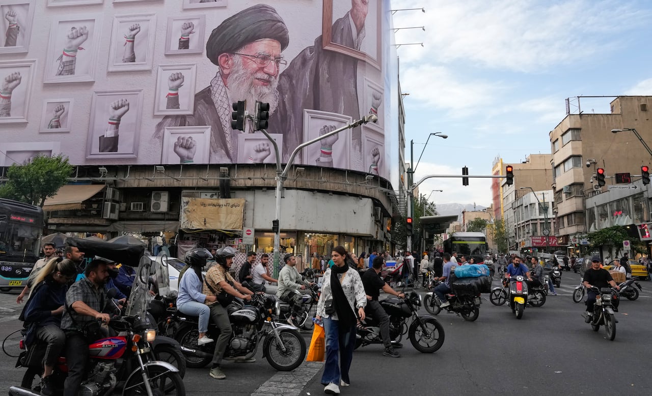 A woman crosses a street with many motorbikes, under a billboard showing Iran's late supreme leader Ali Khamenei and images of clenched fists.