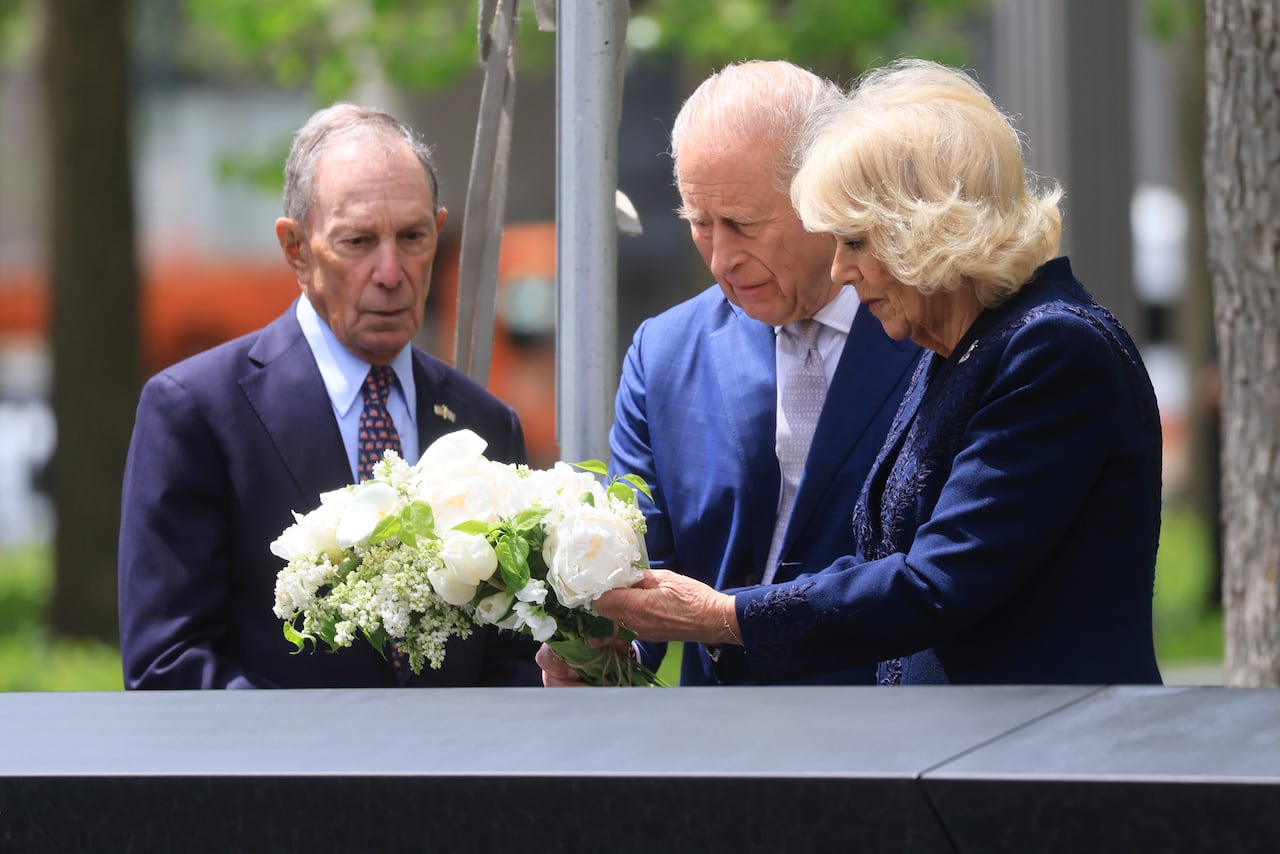 Two men and a woman stand by a stone monument and place a bouquet of white flowers on it.