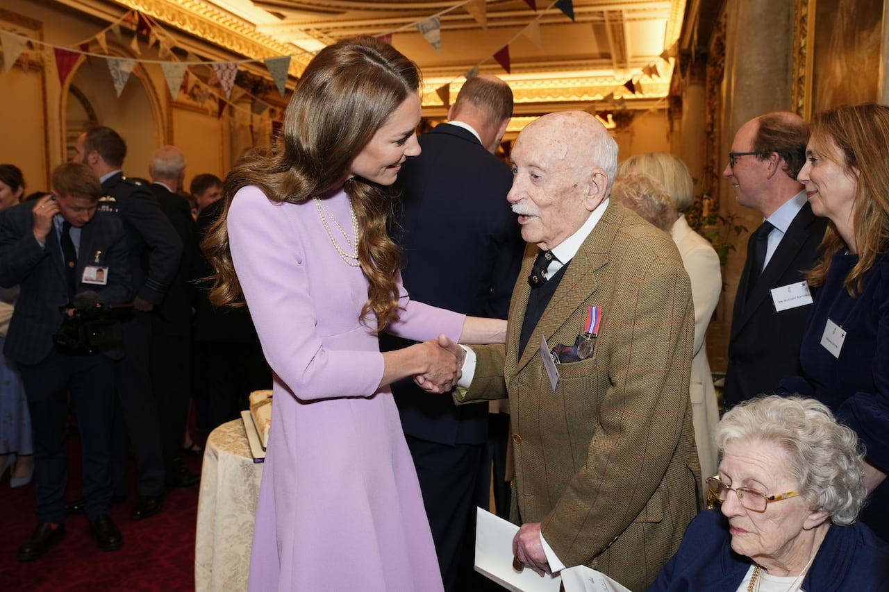 Two people shake hands at a crowded reception.