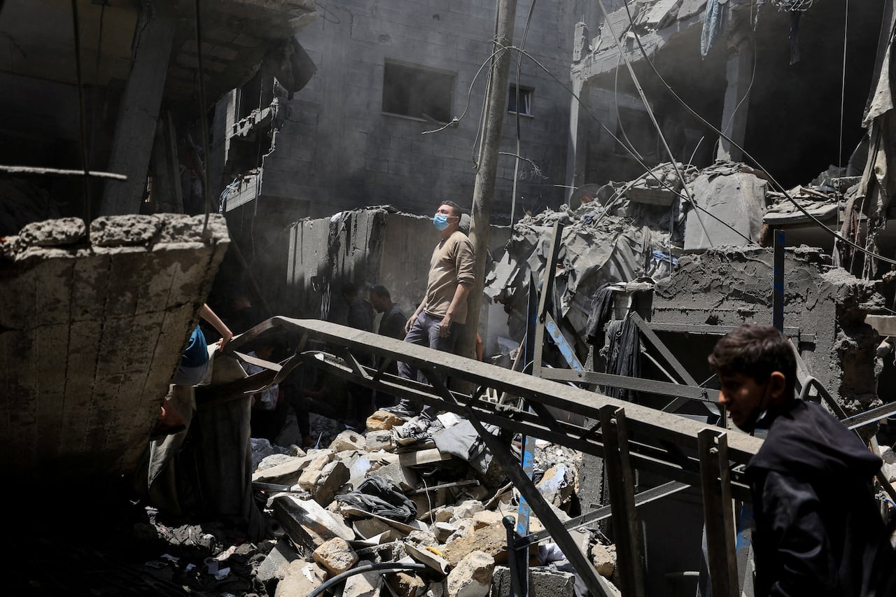 A man wearing a face mask stands in the midst of rubble as he looks up.