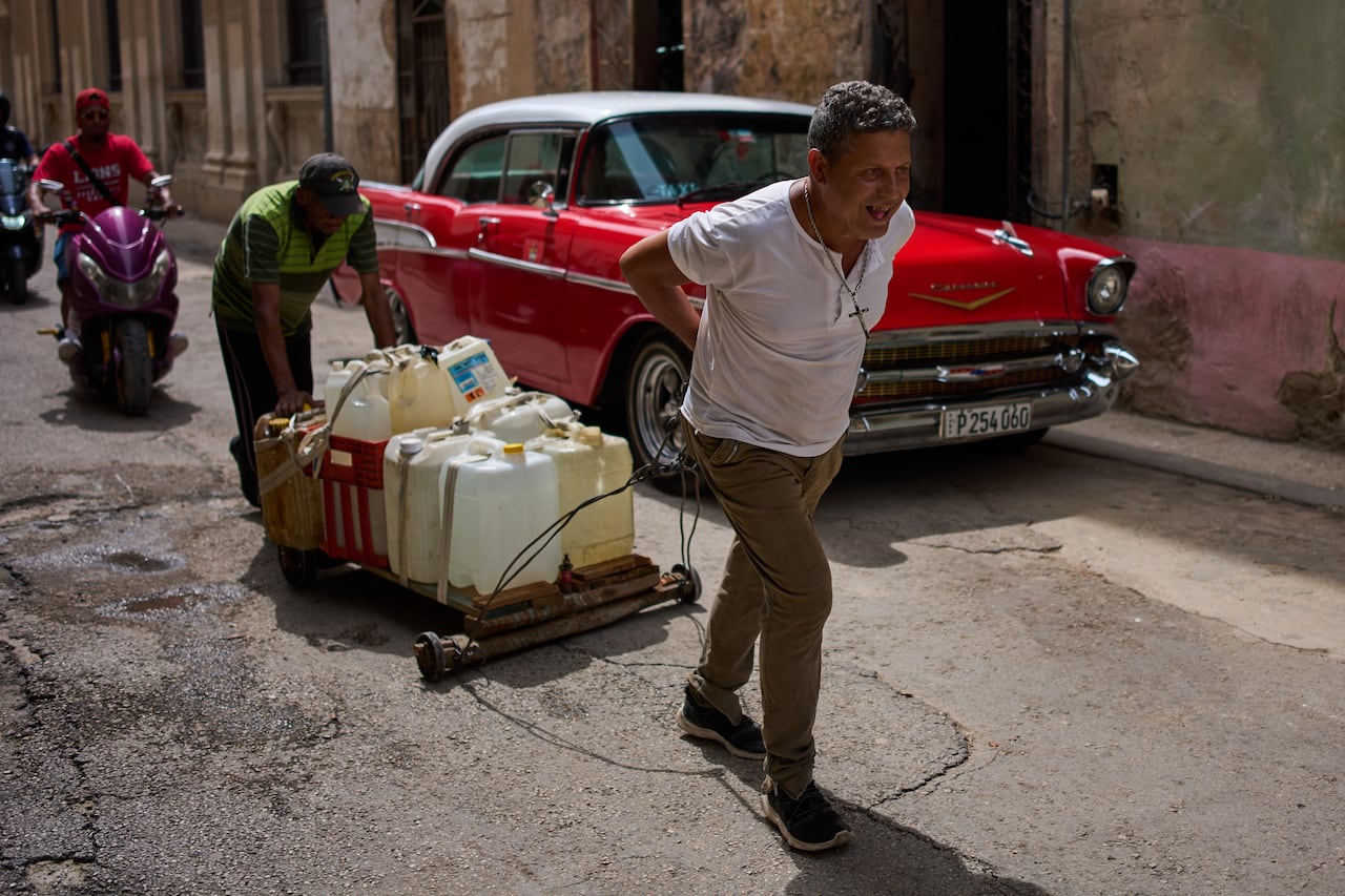 People pull a collection of water containers along a street in Havana.