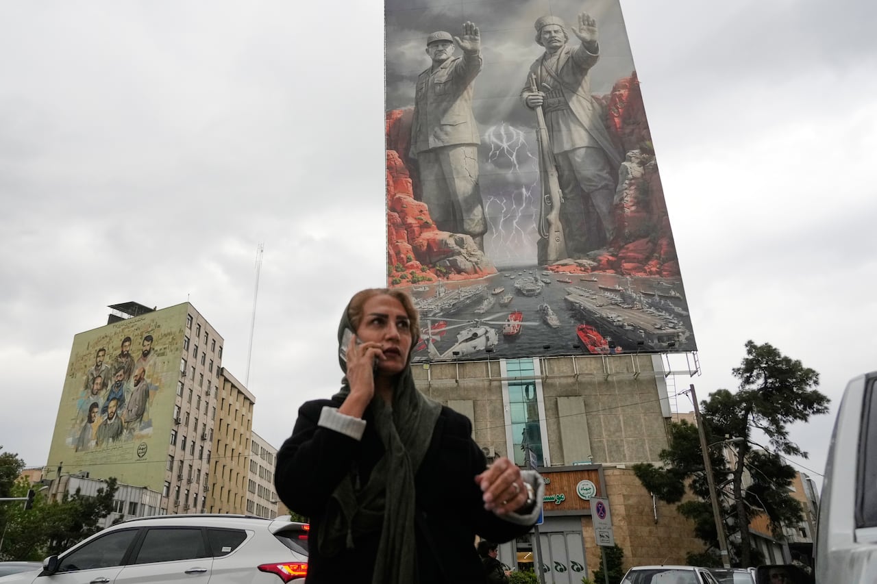 A woman speaks on a cellphone on the street with a military billboard behind her.