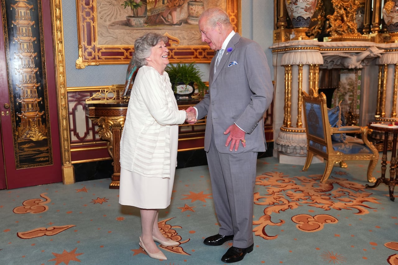 Two people shake hands in a room that includes a large fireplace.