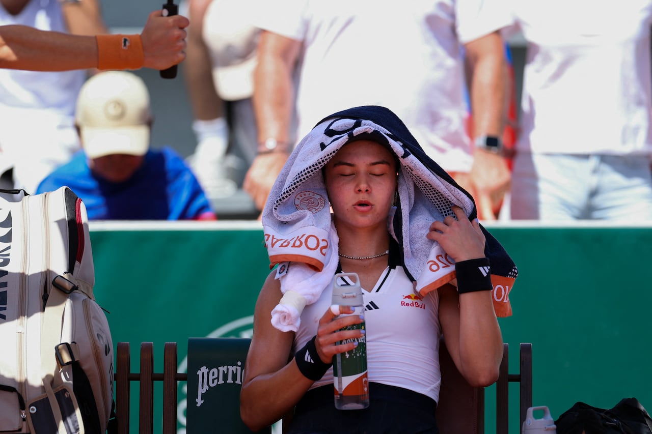 A woman sits, her eyes closed, with a towel over her head and a water bottle in her hand.