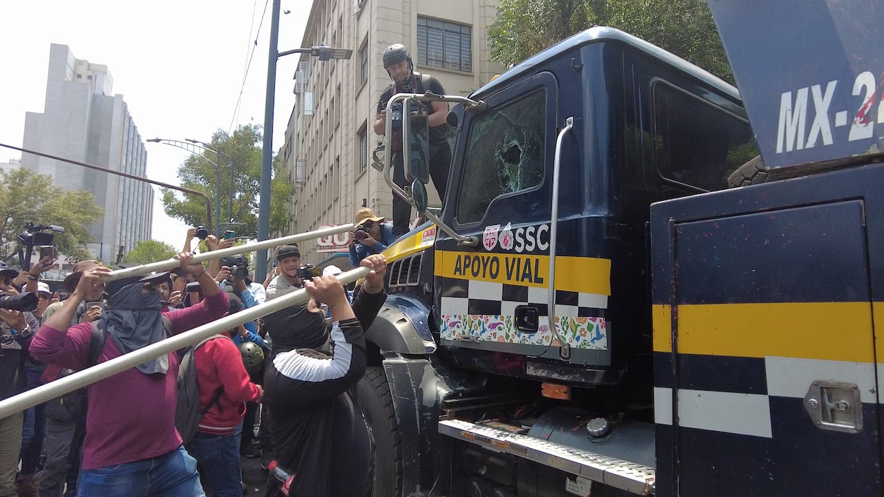 Masked men with pipes swing against the side of a tow truck, smaghing a window.