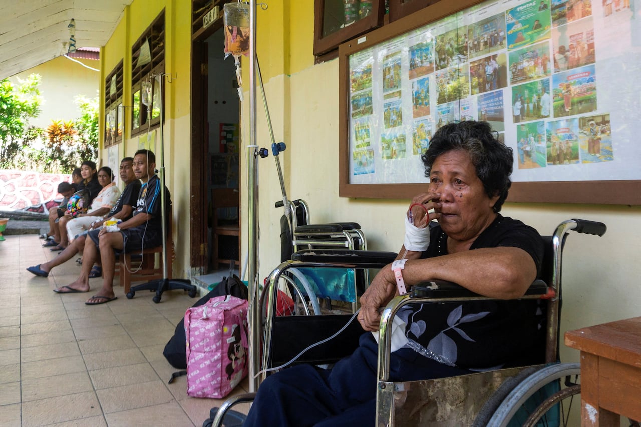 A woman sits in a wheelchair outside a building  with a bandage wrapped around her hand.