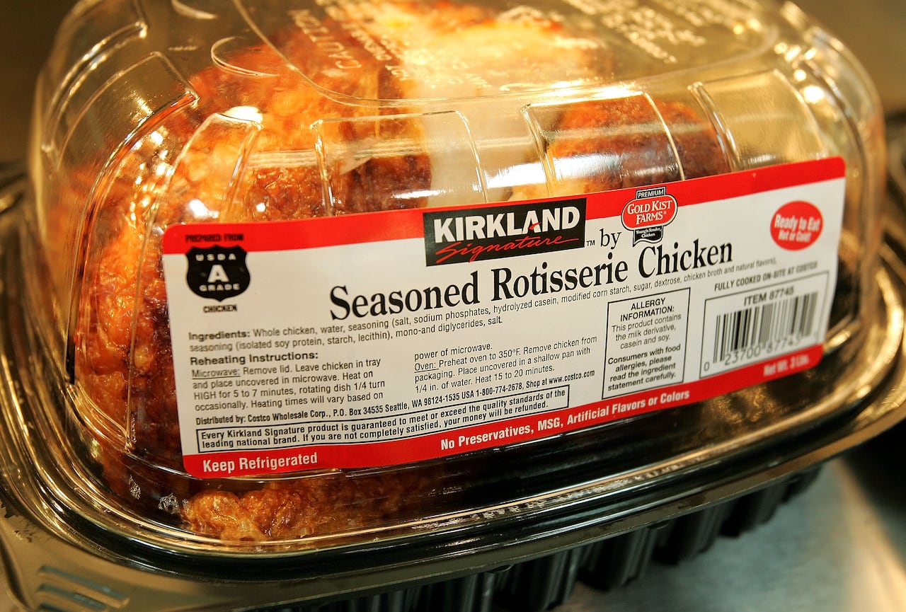 A whole chicken in clear plastic container that includes the label "KIRKLAND Signature Seasoned Rotisserie Chicken".