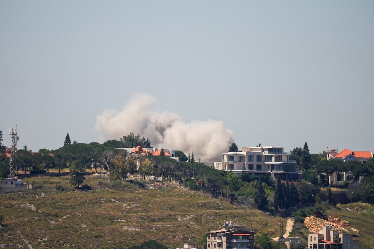 Clouds of grey smoke are shown from a distance in the sky over a settlement of what appears to be residential structures.