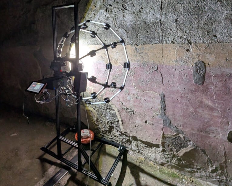 A bright light encased in a metal and wire stand shines on a wall.