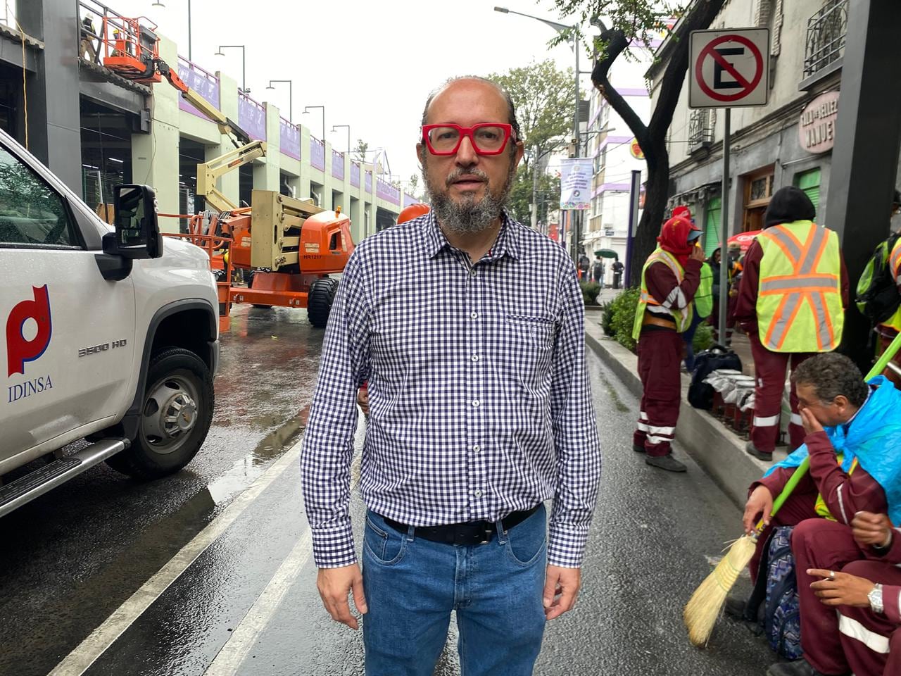 A man with a checkered shirt stands on a street surrounded by construction.