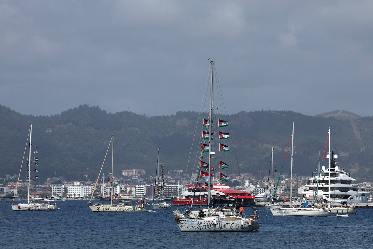 Sailing boats with red, white, black, white and green flags seen on the water.