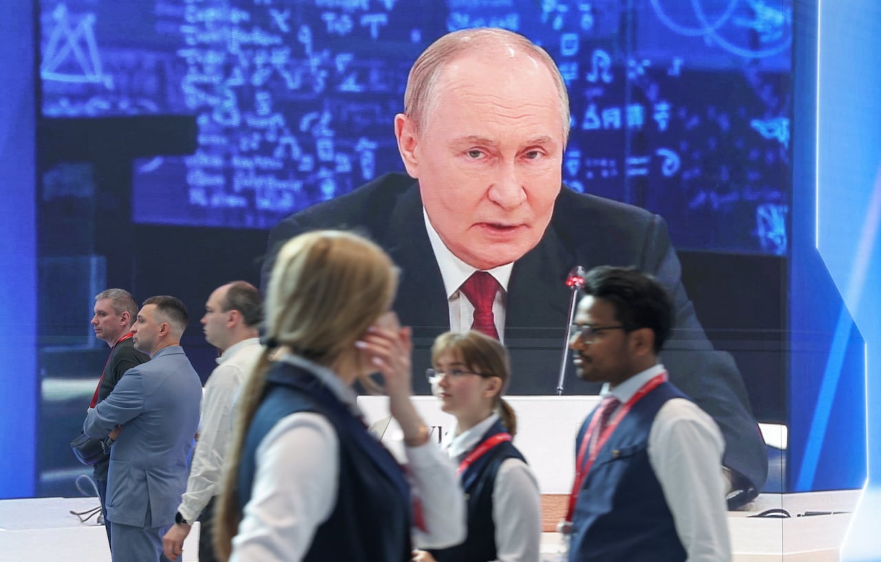 People walk past a screen showing Russian President Vladimir Putin.