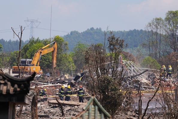 A backhoe can be seen operating at the site of a burned out structure, which was the scene of an explosion at a fireworks plant.