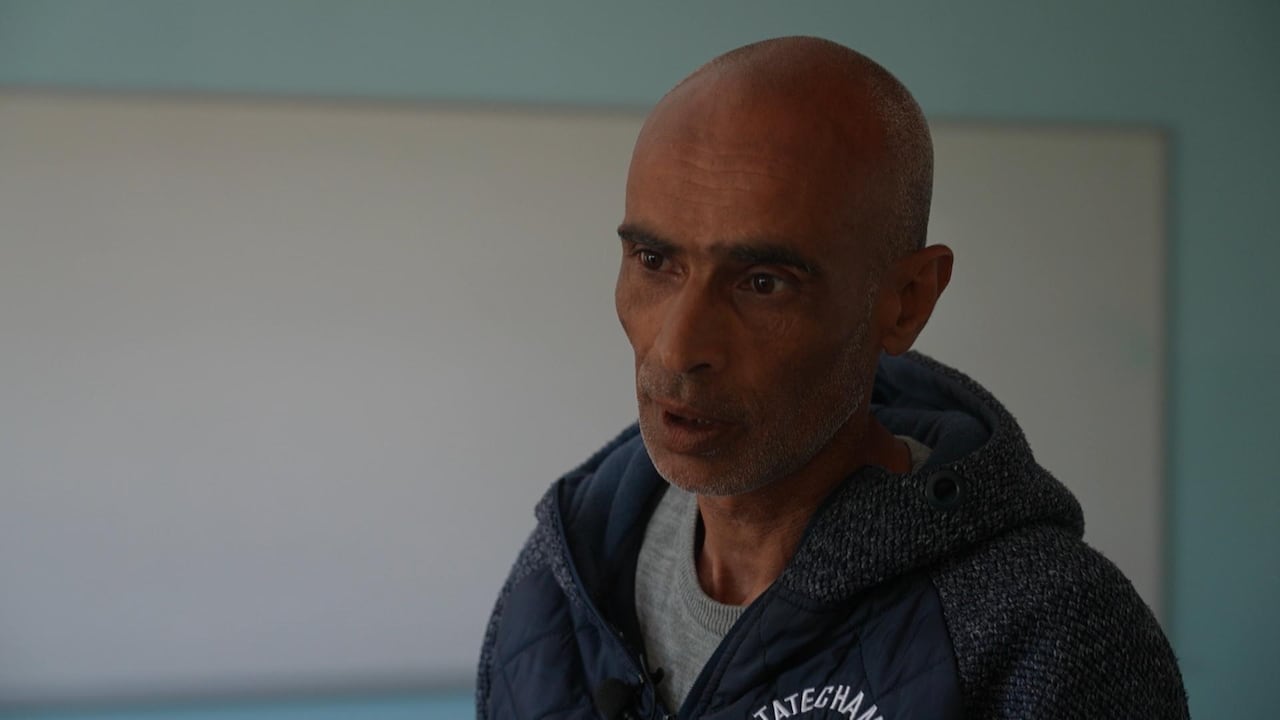 A man in a grey jacket speaks.
