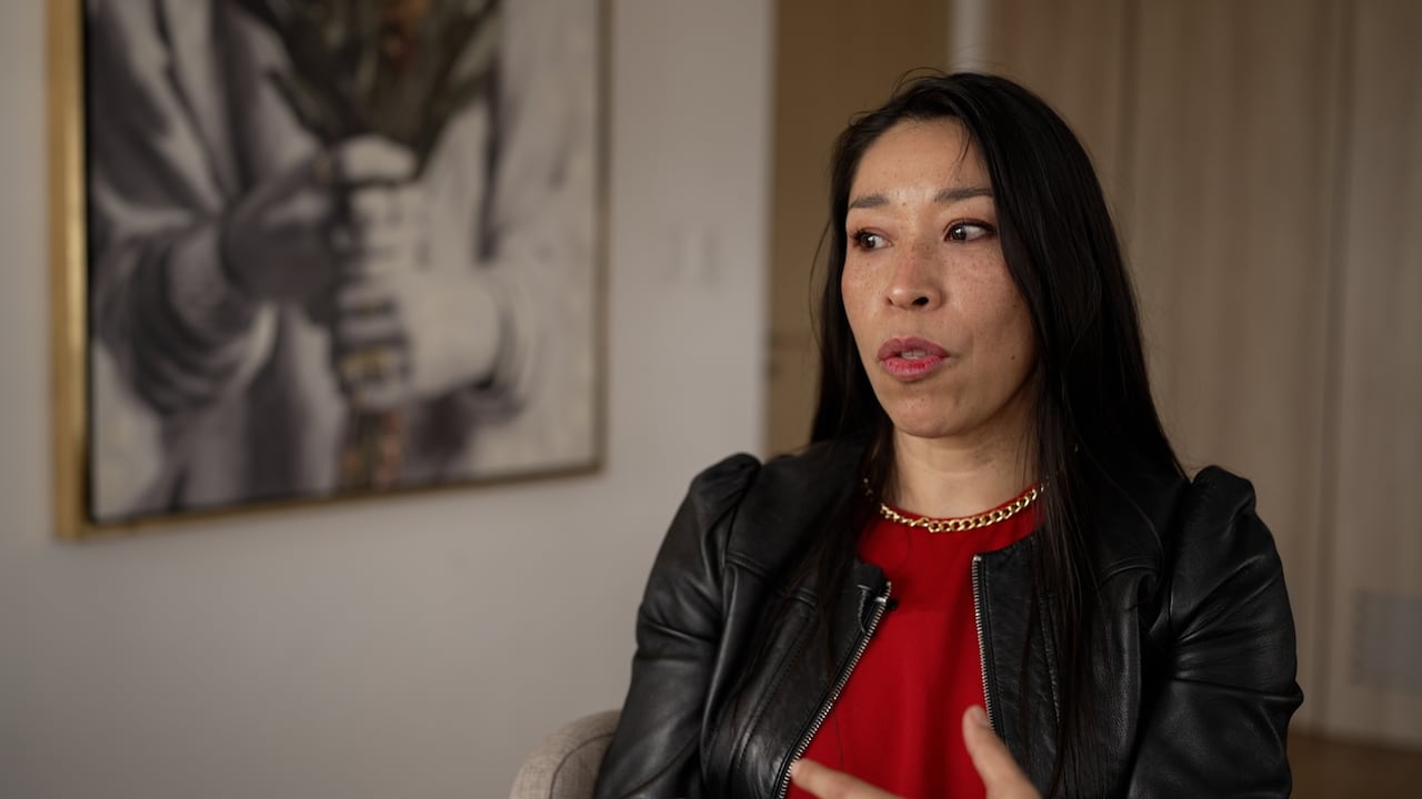 A woman looks past hte camera while making a motion with her left hand.
