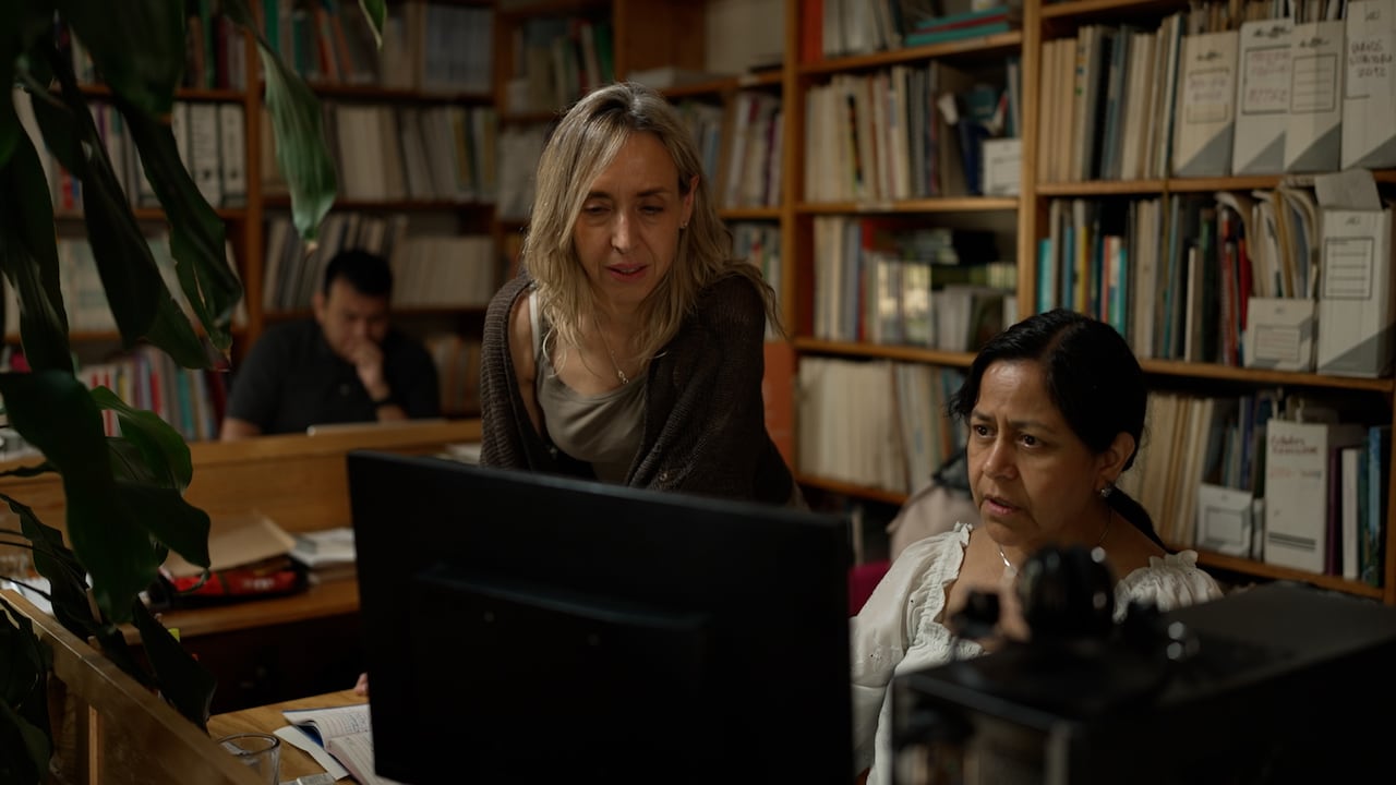 A woman looks over the shoulder of another woman at a computer.