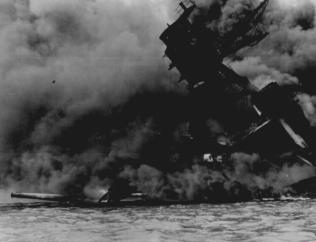 A black and white photo of a battleship burning and sinking.
