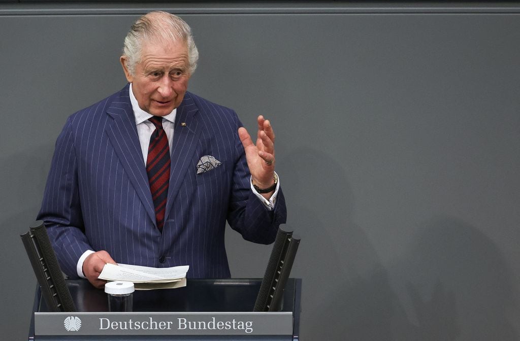 A person gestures with their hand as they deliver a speech while standing behind a podium with a microphone.