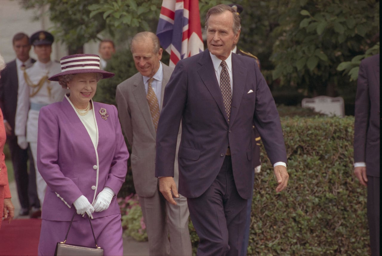 Two people stand beside one another as they walk in front of others.