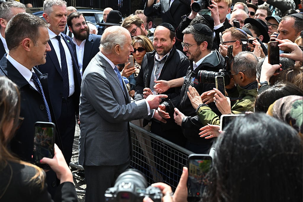 A person shakes hands with another person standing in a crowd behind a barricade/