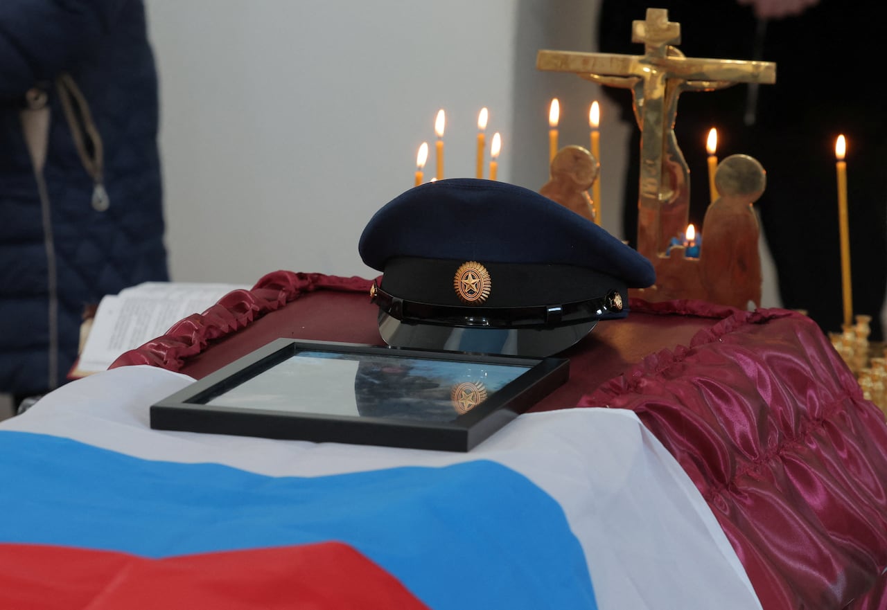 A photo shows a coffin with a Russian flag and military cap.