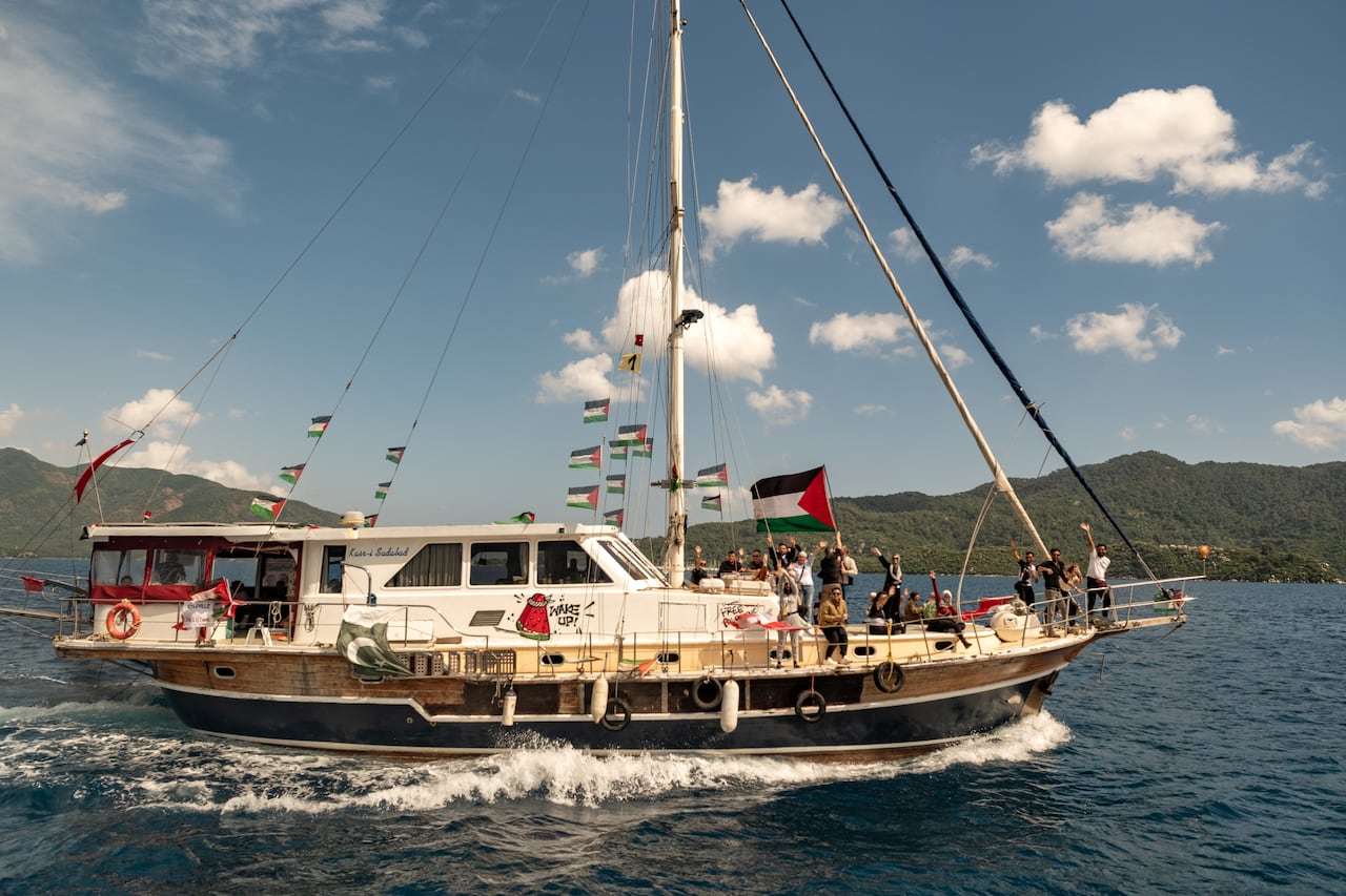 A boat carrying several people on the deck and adorned with flags on its mast is shown.