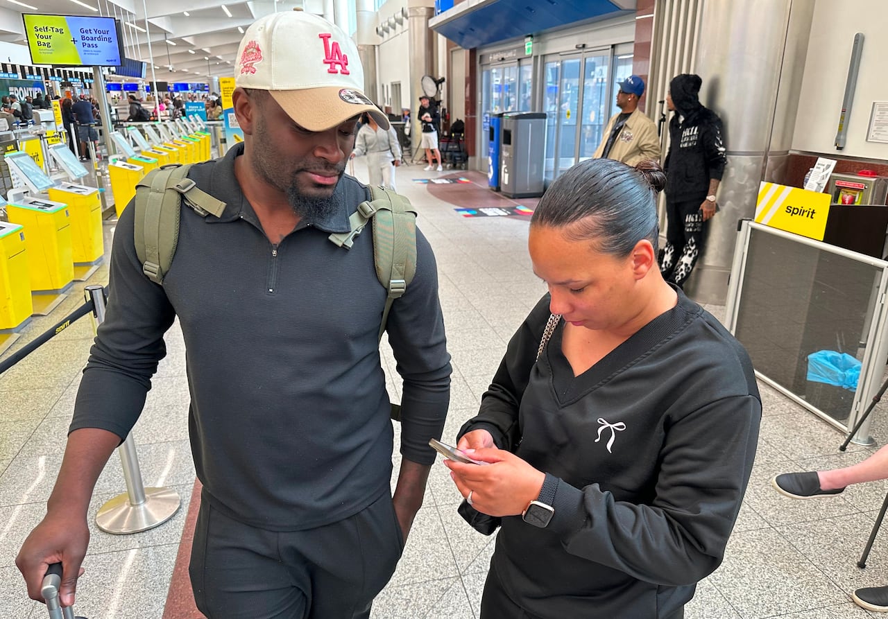 A man and a woman stand near an entrance at an airport while the woman looks at her phone.