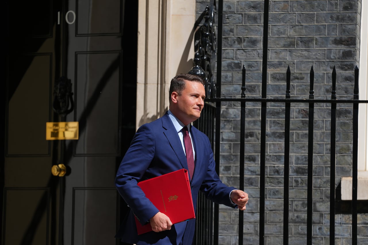 A cleanshaven man with a leather folder under his arm departs the door of a building.