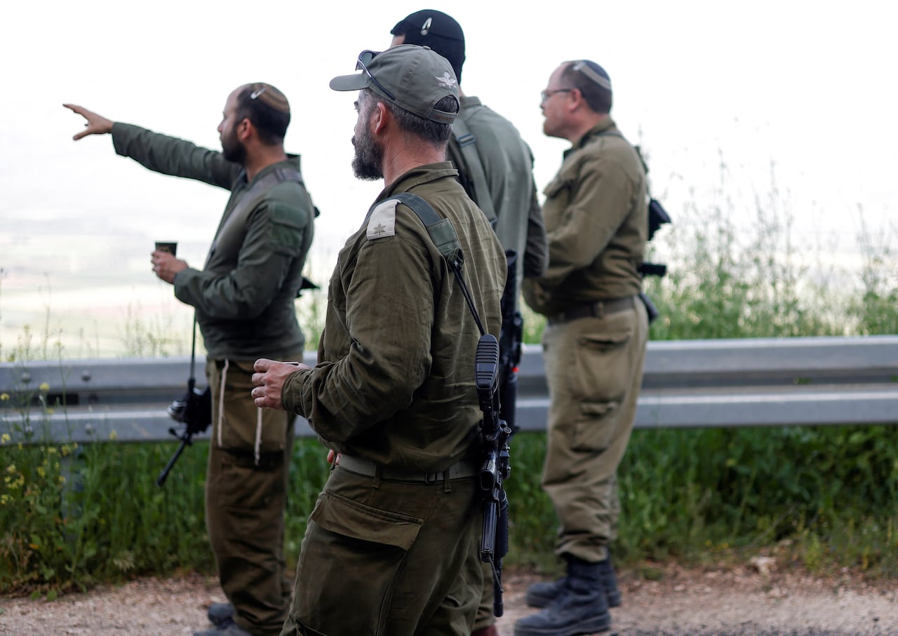 A group of Israeli soldiers standing near a barrier and looking in the same direction in the distance