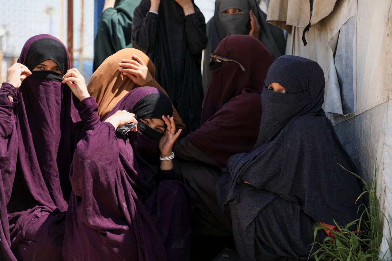 Women wearing burqas sit on the ground at a tent camp.