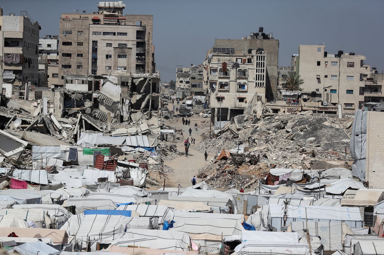 A crowded tent camp is seen near destroyed residential buildings.