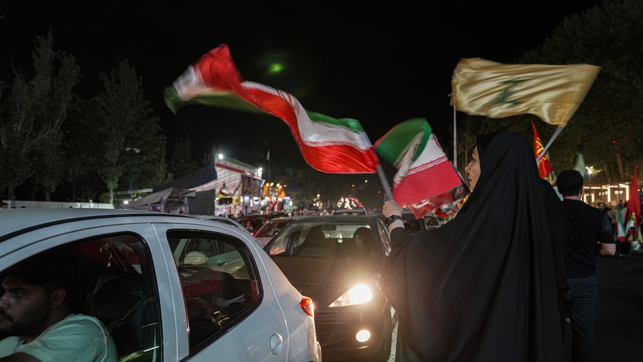 A woman waves a flag as a car drives by at night.