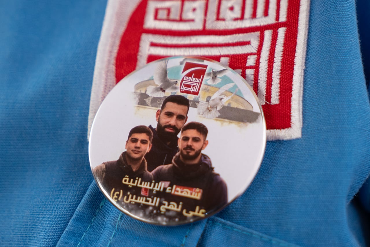 A close up of a circular pin with arabic writing features a photo of three men in paramedic uniforms smiling.