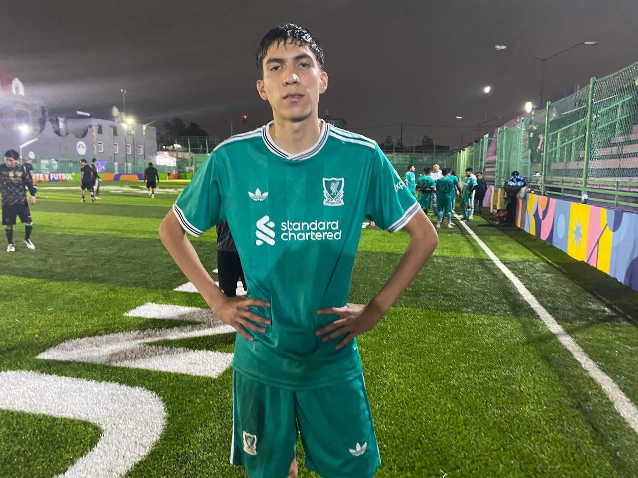 A young man stands looking into the camera dressed in a green soccer uniform.