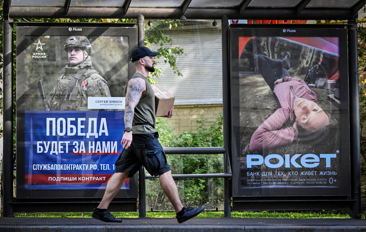 A man carries a box, while walking by a pair of posters — one promoting contract military service — in Moscow.