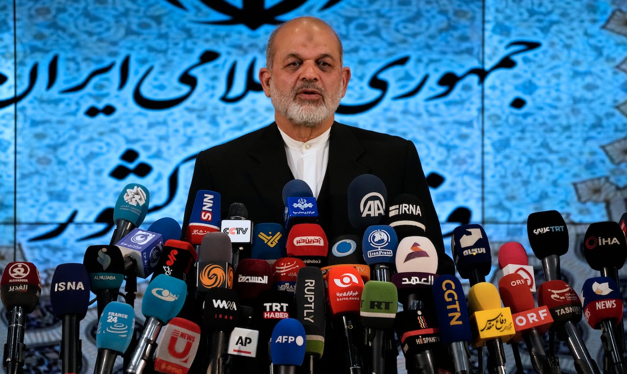 Ahmad Vahidi stands in front of a monitor showing text in Farsi, with more than two dozen microphones in the foreground.