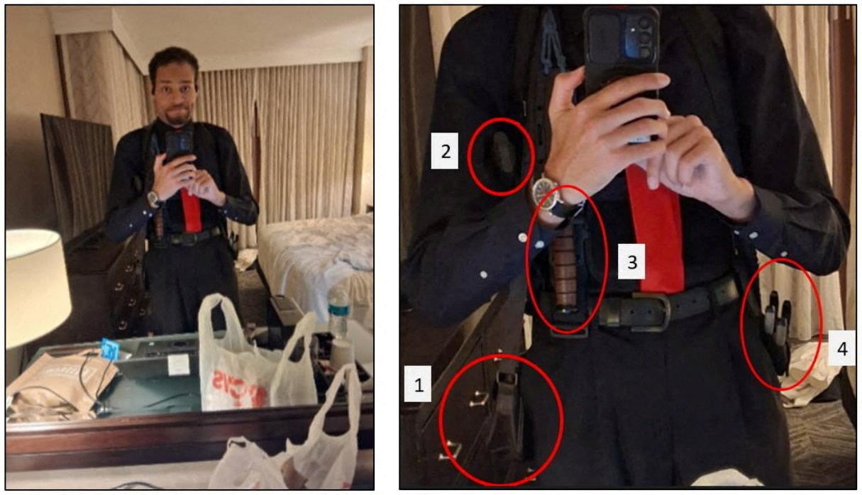 A man in a black shirt, black pants and red tie takes a photo of himself in a mirror. There is a knife and a bag of ammunition strapped to his body.