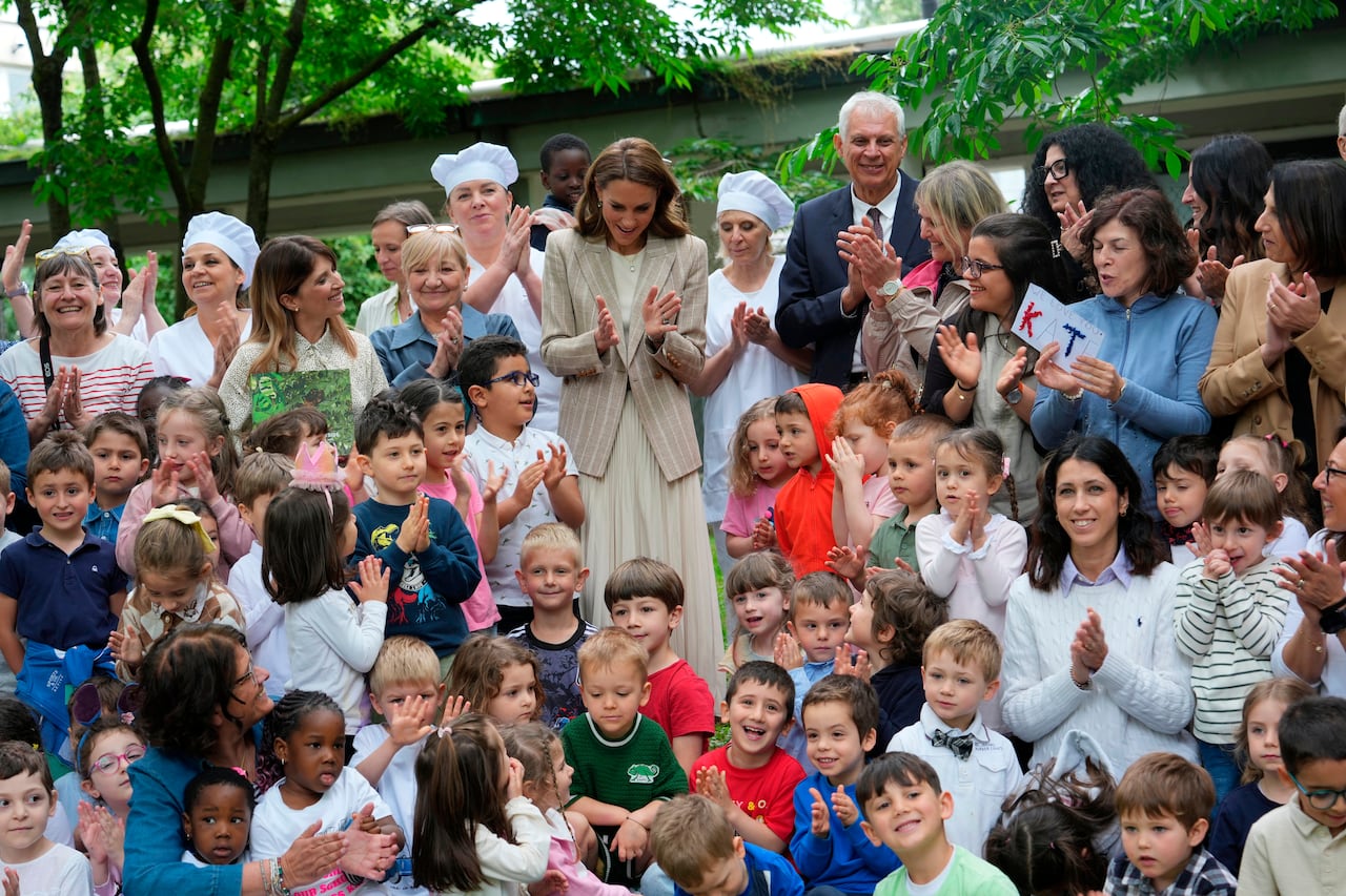 Adults standing clap as children seated in front of them clap, too.