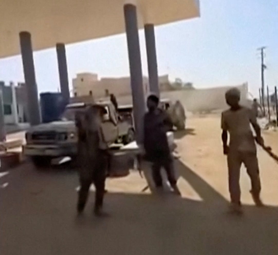 Group of armed man stand around at a gas station in the desert.