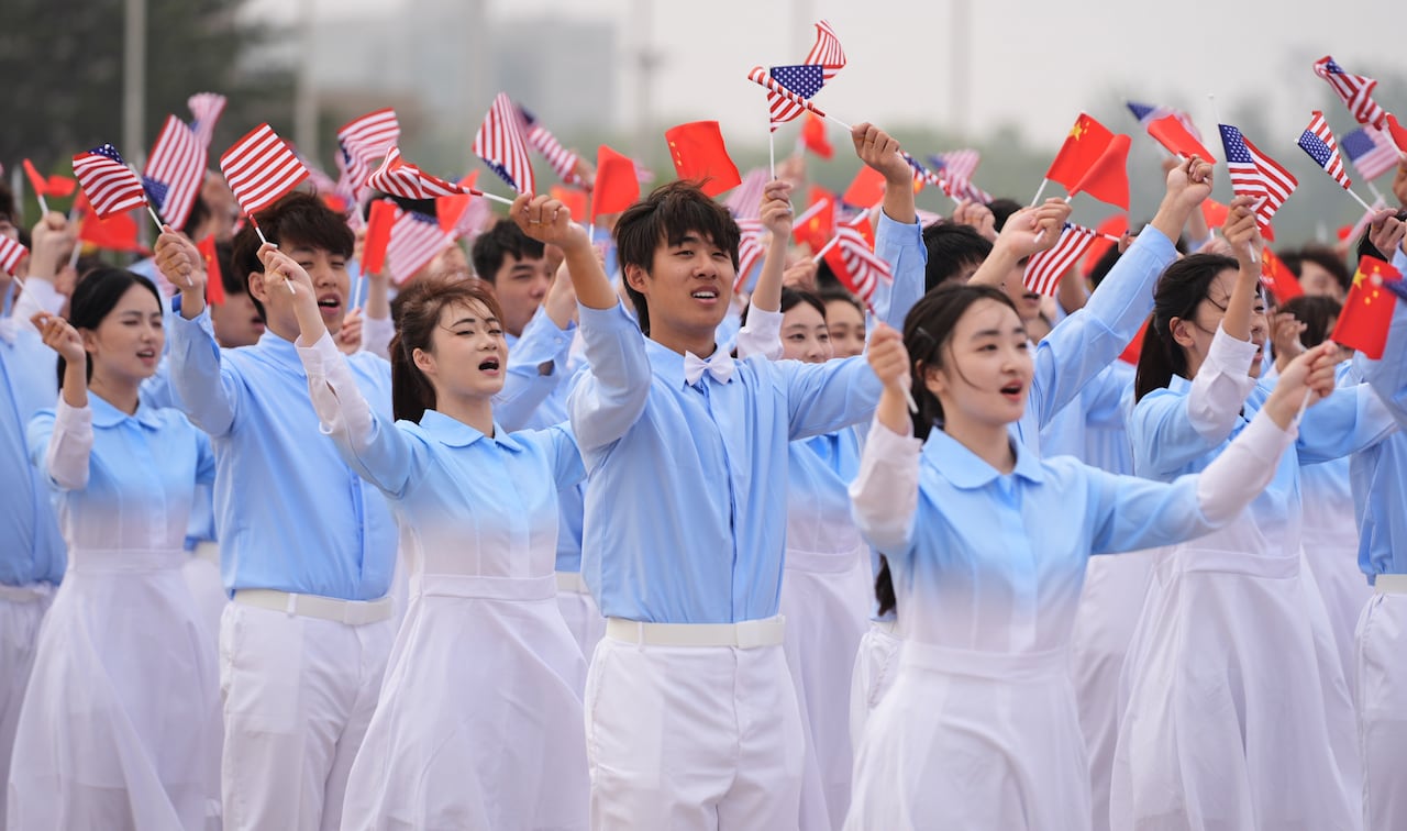 A group of young men and women dressed wearing outfits in pale blue and white wave small Chinese and American flags,