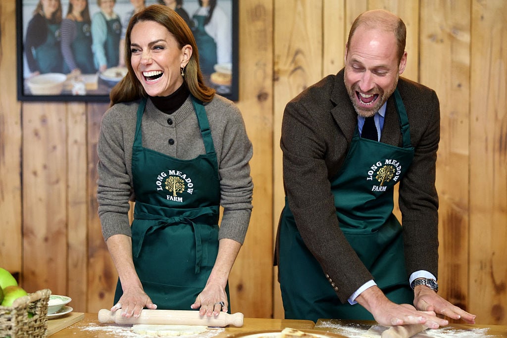 Two people laugh while rolling dough on a table.