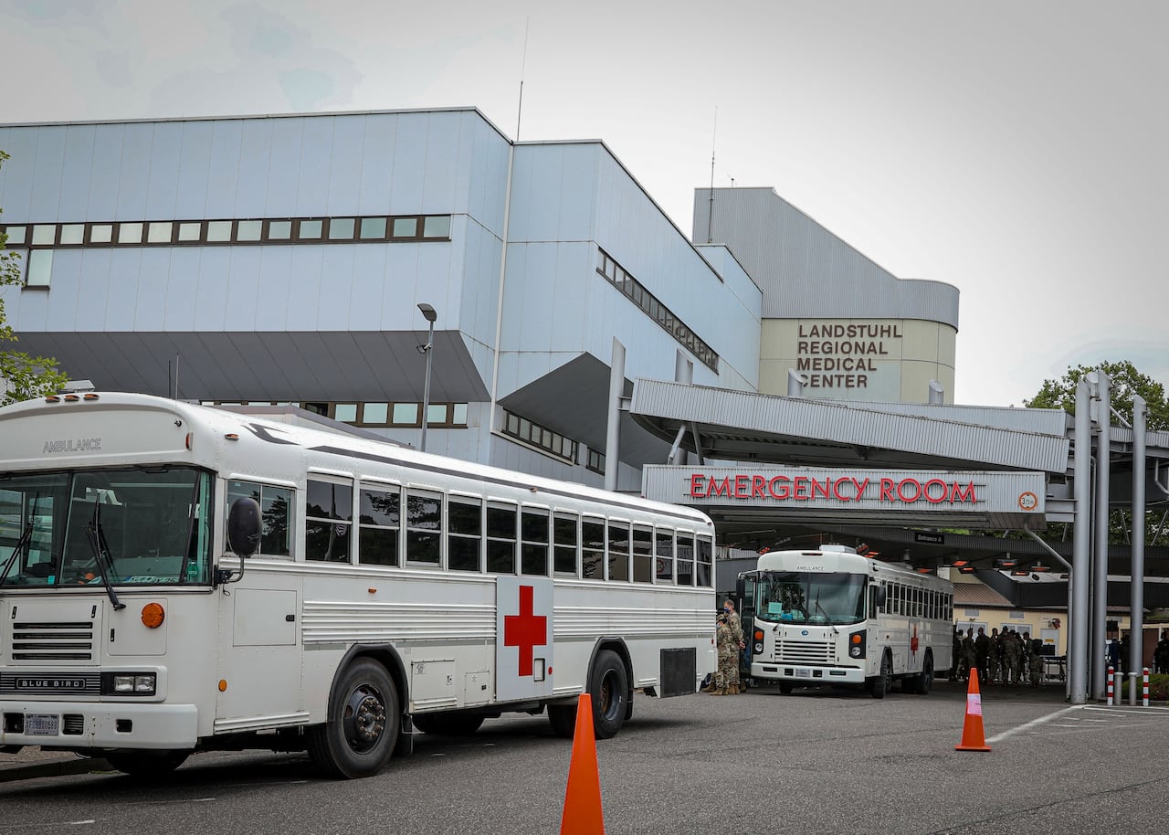 Two large white buses outside a hospital building.