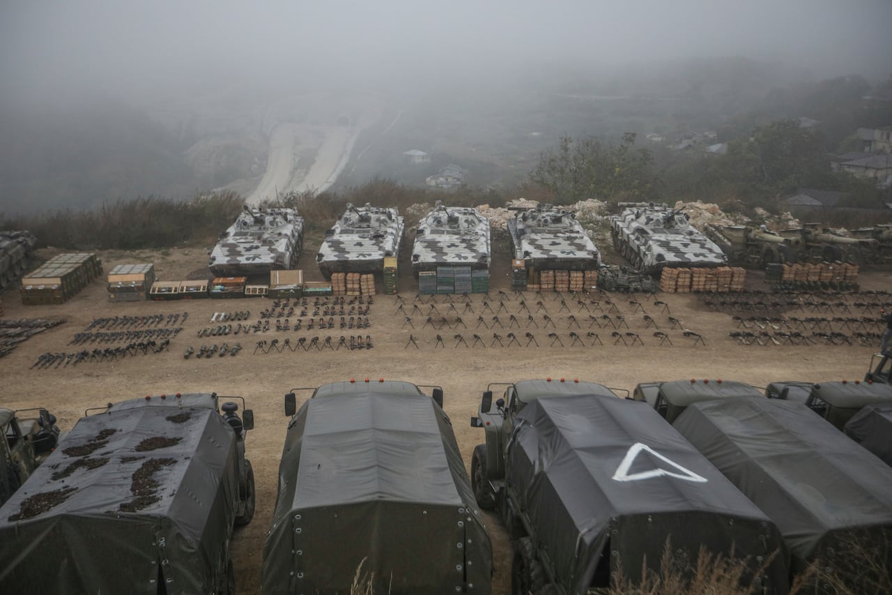A wide shot of military tents and vans with weapons lined up in between them on the dirt.