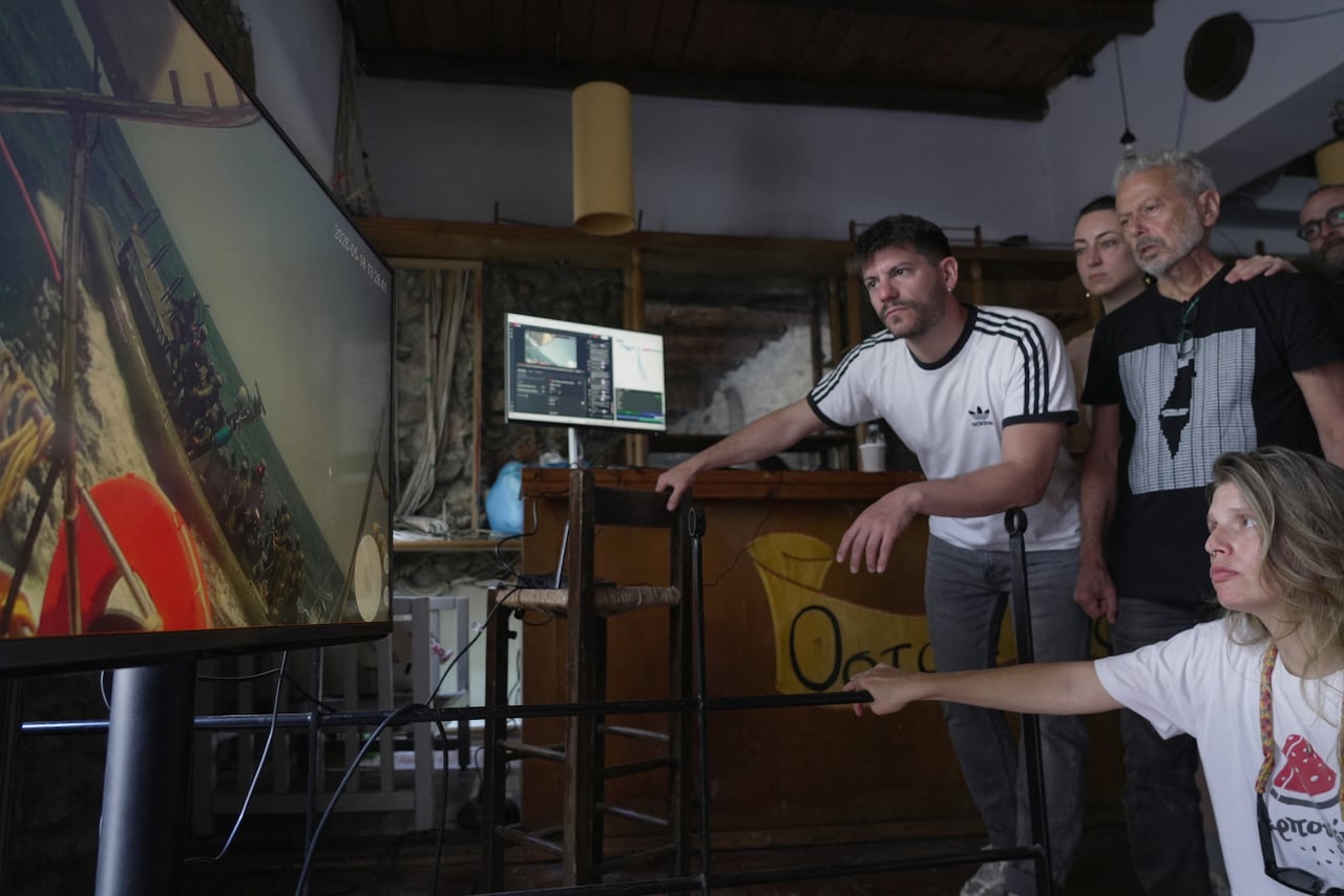 A group of people watch a video transmission of a boat on a television.