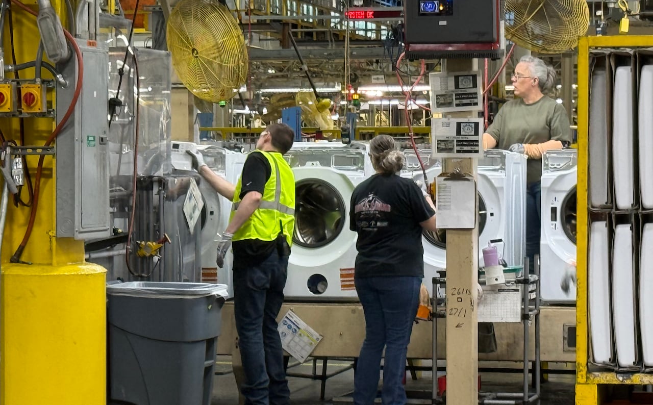 Three assembly line workers and some partially assembled washing machines in a factory.