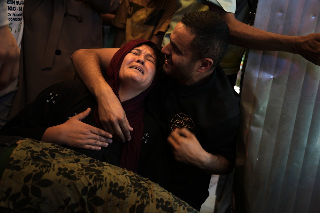 A woman in a burgundy head scarf cries as a man holds her.